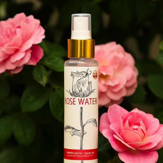 Bottle of rose water with a gold cap against a background of pink roses.