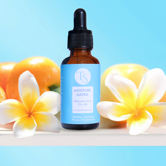 Bottle of 'Moisture Matrix' with plumeria flowers on a blue background