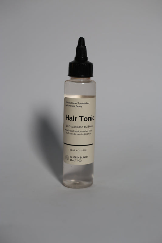Hair Tonic bottle with open dropper, placed beside natural ingredients like herbs or oils.