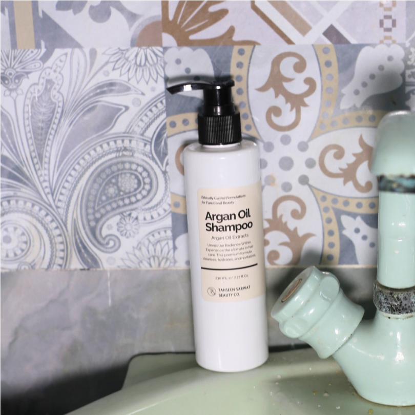 Argan Oil Shampoo bottle placed beside a wooden comb, towel, and dried flowers.
